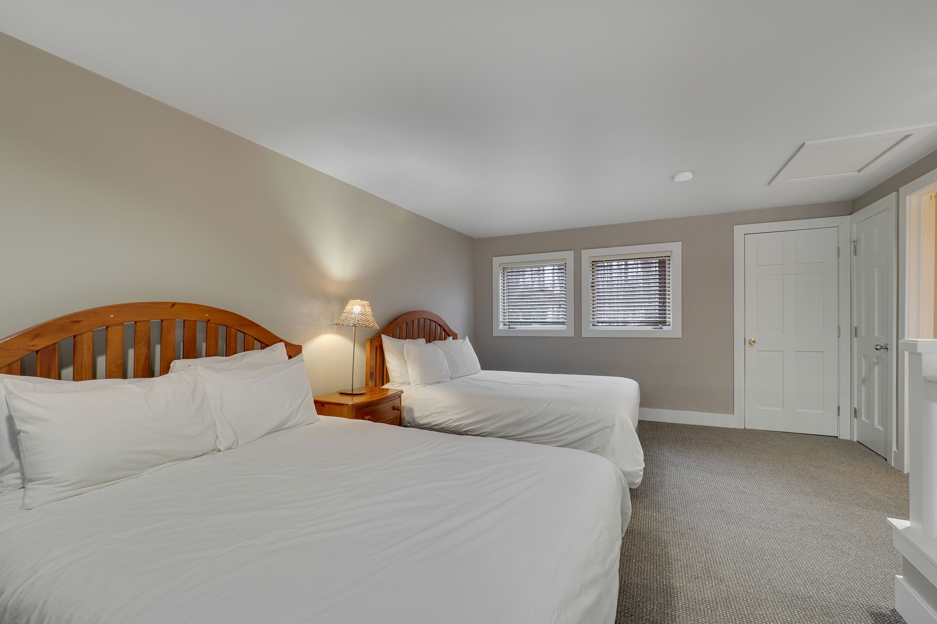 A bedroom with two beds, a nightstand with a lamp, and a door.