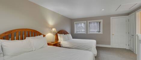 A bedroom with two beds, a nightstand with a lamp, and a door.