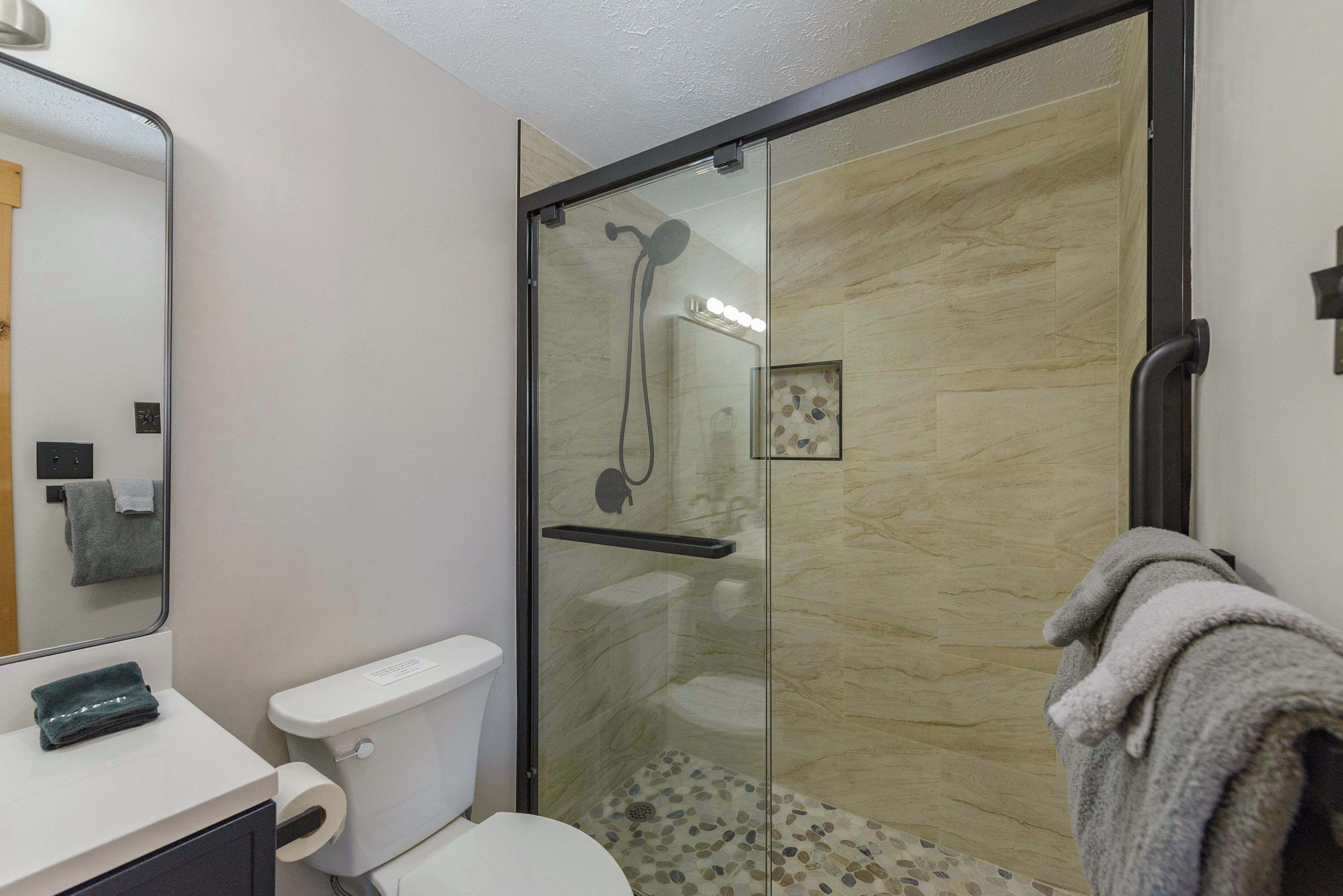 A modern bathroom with a glass-enclosed shower, a toilet, and a sink with a towel.