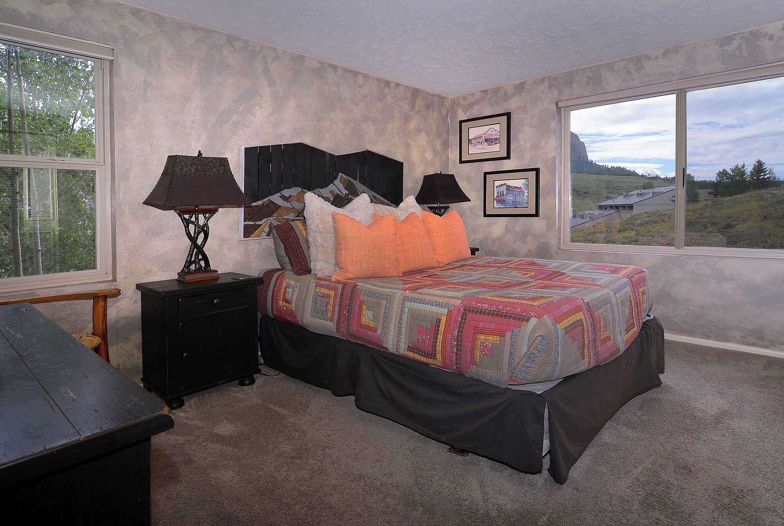 A bedroom with a bed, two bedside tables, a window with a view of a landscape, and a door.