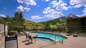 A hot tub area with a sign listing rules, surrounded by lounge chairs and a pool. - The Bluebell, Chateaux Condo, Pool, Hot tub, Sauna (Mt. Crested Butte)