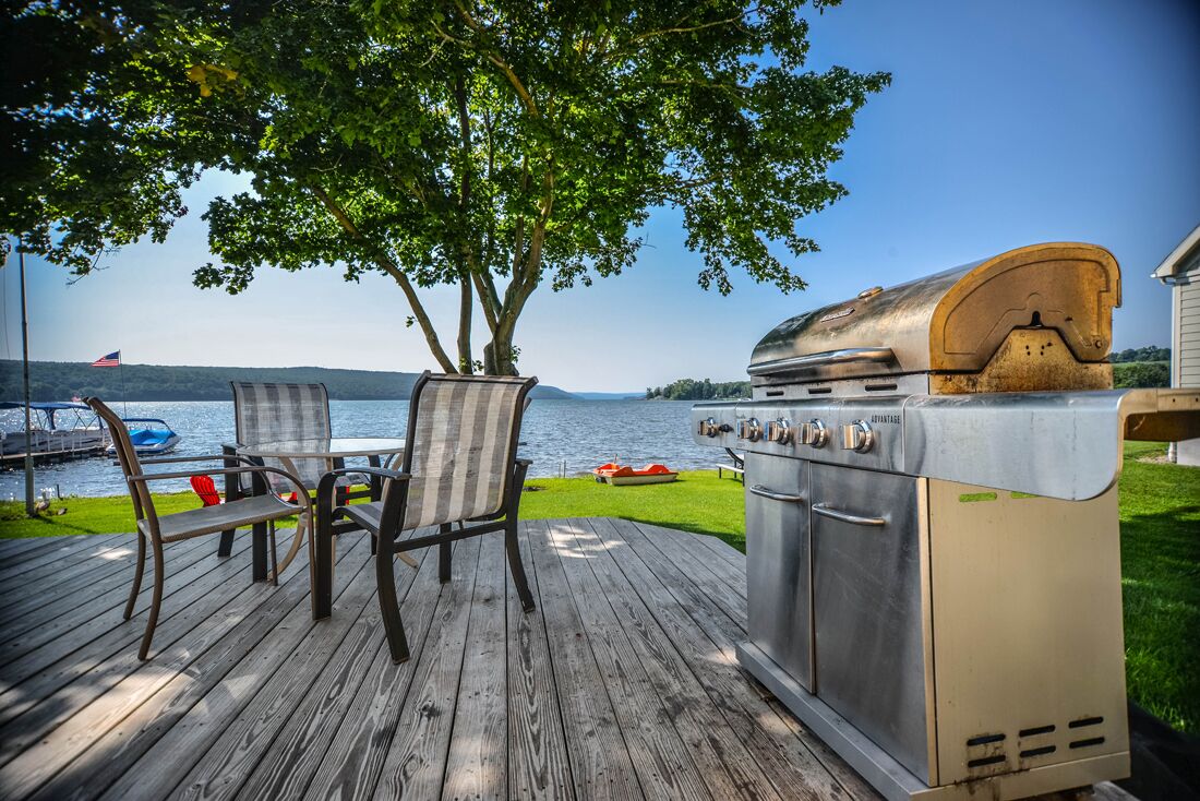 Une terrasse avec un barbecue, des chaises et une vue sur un lac.