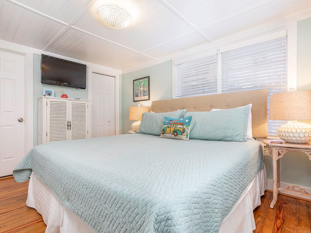 Een slaapkamer met een bed, een televisie aan de muur, een raam met zonwering, en een nachtkastje met een lamp.