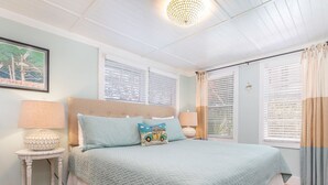 Un dormitorio con una cama grande, dos mesitas de noche, una lámpara en el techo y una ventana con persianas.