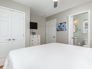 A bedroom with a large bed, a dresser, a television, and a painting on the wall. - The Flying Pigs Cottage | Pet Friendly, Fire Pit! (Tybee Island)