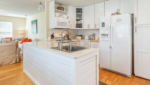 Een moderne keuken met witte kasten, een inbouw eiland met een spoelbak, een koelkast en een magnetron.