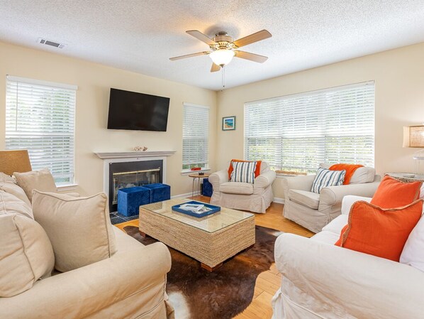 A living room with a fireplace, multiple sofas, a coffee table, and a ceiling fan. - The Flying Pigs Cottage | Pet Friendly, Fire Pit! (Tybee Island)