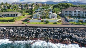 A coastal hotel with a rocky shoreline, multiple buildings with balconies, and a clear view of the ocean.