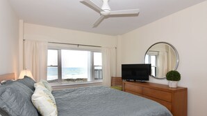 Un dormitorio con cama, televisión, cómoda, espejo y vista al mar.