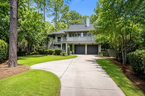 A two-story house with a covered front porch, a driveway leading to a garage, and a well-maintained lawn. - 16 Painted Bunting - Oceanfront Home with Private Pool & Spa. (Hilton Head Island)
