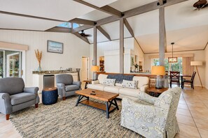 A spacious living area with a sofa, armchairs, and a coffee table. There is a kitchen area with a sink and cabinets, and a dining area with a table and chairs.