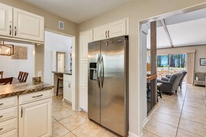A modern kitchen with white cabinetry, a stainless steel refrigerator, and a dining area with a view.