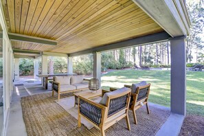 A covered patio with wooden furniture, a grill, and a view of a landscaped garden.