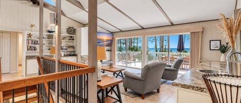A spacious living area with a view of the ocean, a balcony with outdoor seating, and a staircase with a wooden railing.
