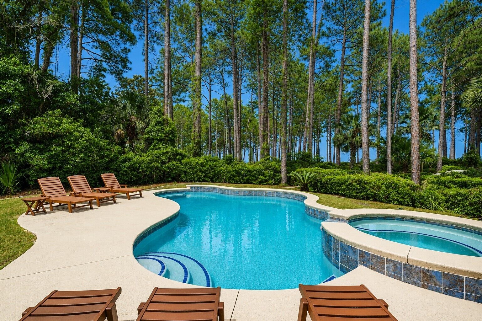 A swimming pool with lounge chairs and a clear view of tall trees.