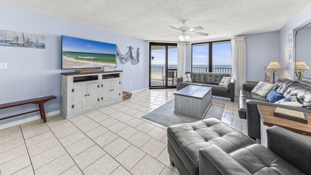 A spacious living room with a large sofa, a coffee table, and a television. There is a balcony with a view of the ocean. - Phoenix VI 811 | Beachfront | Pickleball | Pools | My Beach Getaways (Orange Beach)