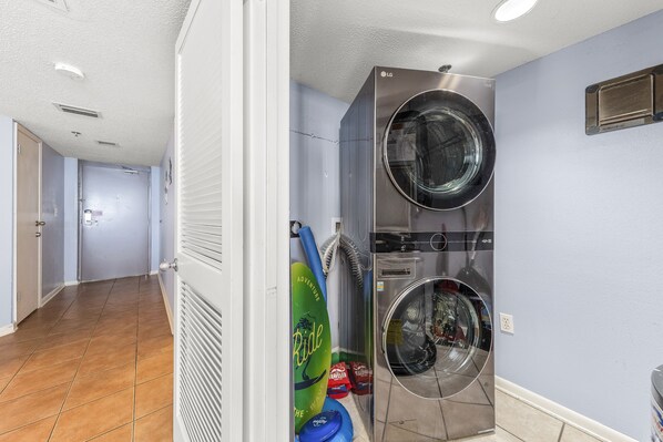 A laundry room with two stacked front-loading washers and dryers, a surfboard, and a blue mat.