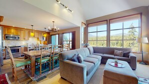 A spacious living area with a large sofa, a dining table with chairs, and a kitchen with wooden cabinets and modern appliances. - 3BR | Blackcomb Greens | Wood Burning Fireplace | Complex Hot Tub | Parking | Mountain Views (Whistler)