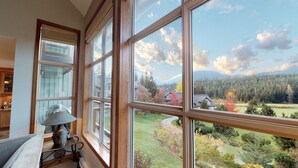 A room with large windows offering a view of a forested area and a mountain in the distance. - 3BR | Blackcomb Greens | Wood Burning Fireplace | Complex Hot Tub | Parking | Mountain Views (Whistler)