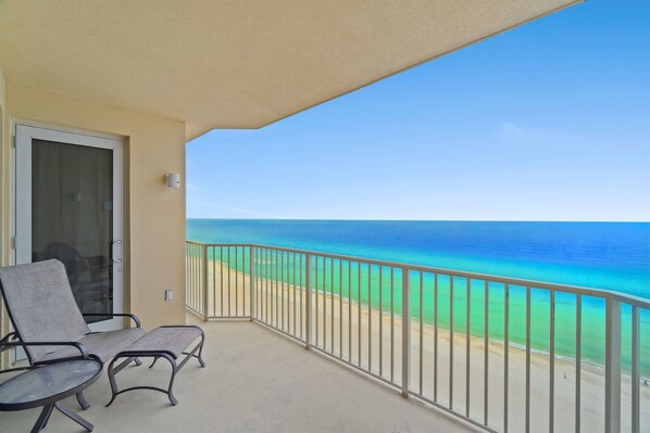A balcony with two chairs and a door, overlooking a beach with clear blue water and a sandy shore. - Boardwalk Beach Resort Family Getaway with Splash Zone and Gulf Views (Panama City Beach)