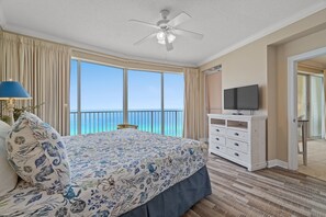 A bedroom with a large bed, a ceiling fan, a TV on a dresser, and a balcony with a view of the ocean. - Boardwalk Beach Resort Family Getaway with Splash Zone and Gulf Views (Panama City Beach)