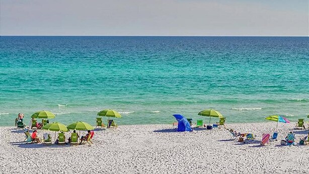 Une plage où des gens se détendent sous des parasols, près d’une tente et de chaises de plage.
