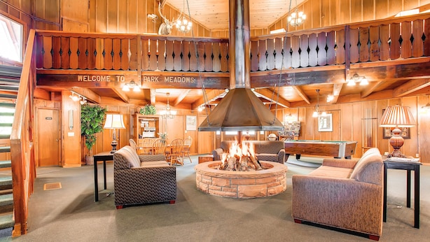 Eine gemütliche Lobby mit einem Steinkamin, bequemen Sitzgelegenheiten und einer Holzbalkendecke mit einem Schild 'Welcome to Park Meadows'.