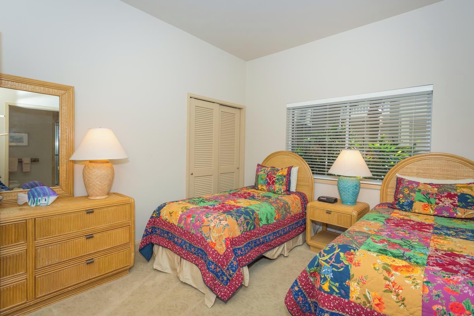 A bedroom with two beds, a dresser, a mirror, and a window with blinds.