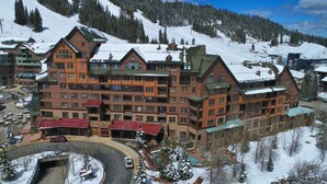 Un grand chalet à étages, un télésiège en arrière-plan et une montagne enneigée.
