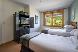 Une chambre d’hôtel avec deux lits, une télévision, une armoire et une fenêtre donnant sur des arbres.