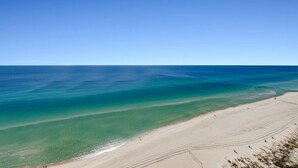 Una playa con aguas turquesas cristalinas, una orilla arenosa y un muelle a lo lejos.