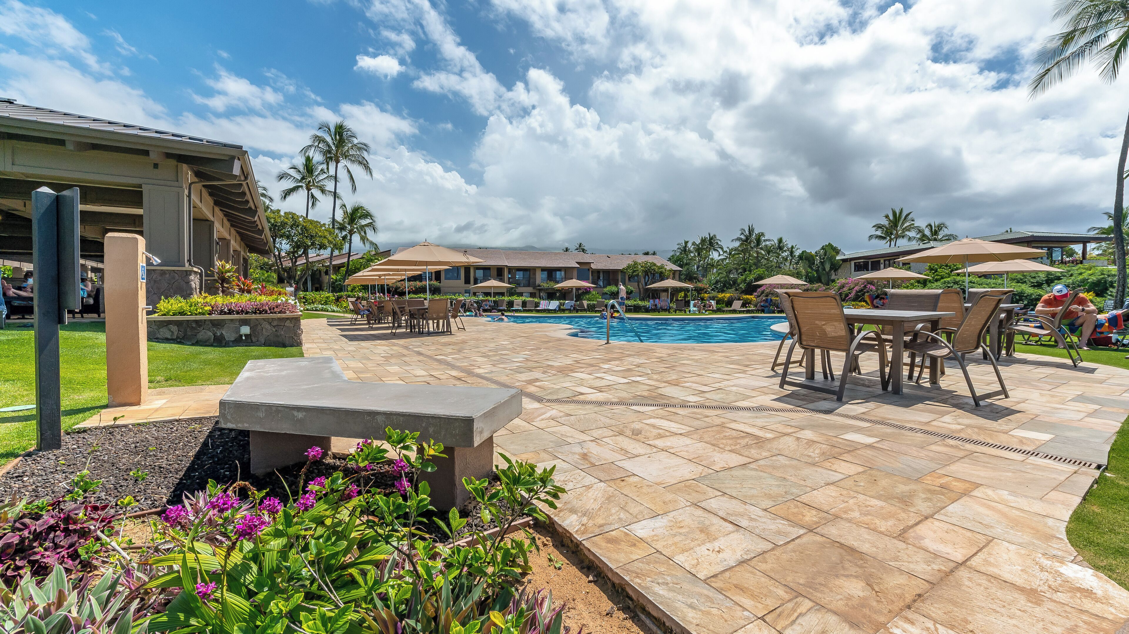 A pool area with lounge chairs and umbrellas, surrounded by palm trees and a clear sky.