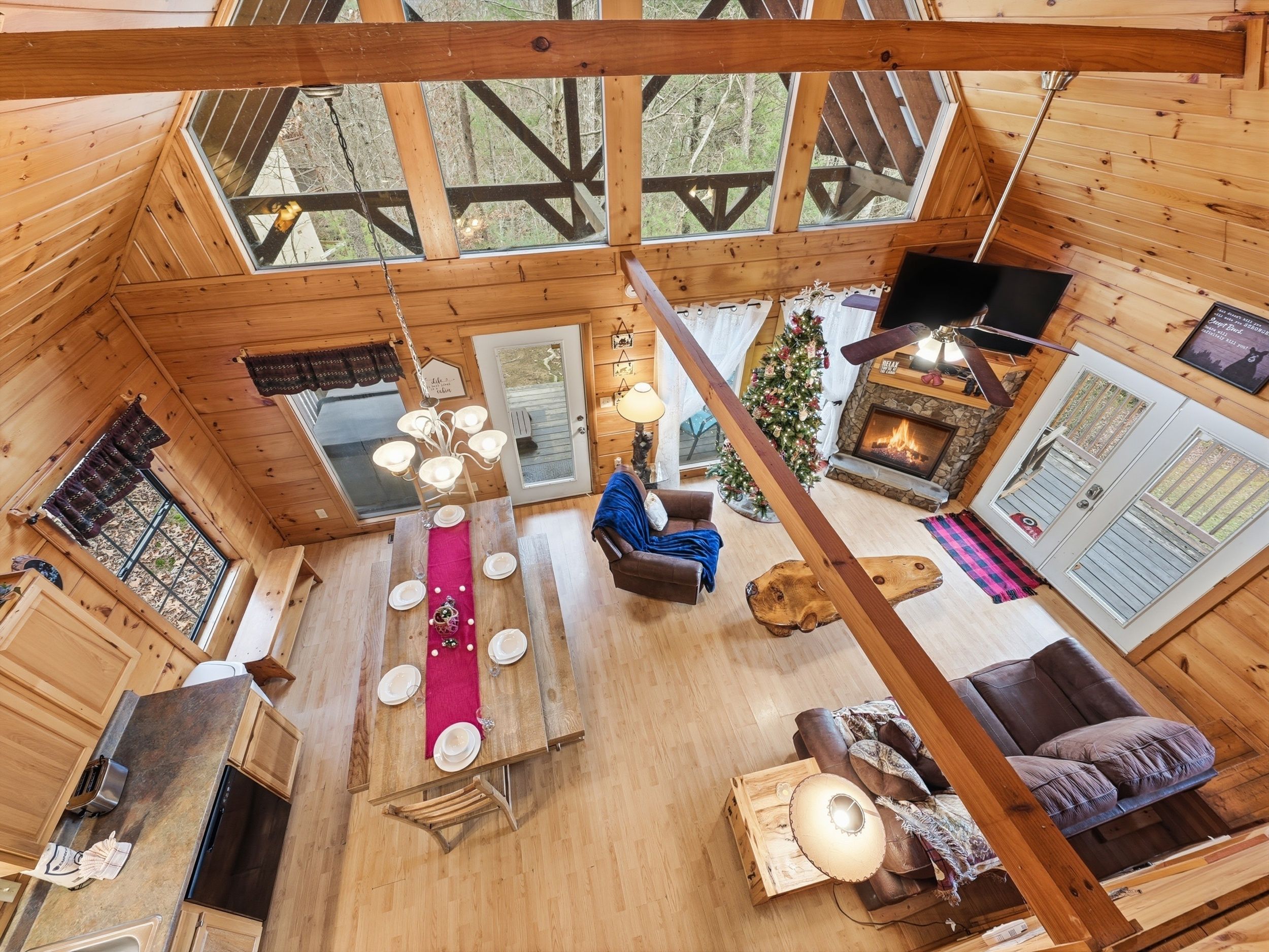 A cozy cabin interior with a dining area, a fireplace, and a large window overlooking the forest.