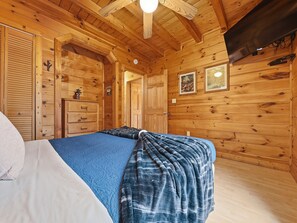 A wooden cabin bedroom with a bed, dresser, and wardrobe. - Hot Tub | Fire Pit | Secluded | Pet Friendly | Pool Table (SEVIERVILLE)