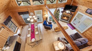 L’intérieur chaleureux d’un chalet comprend un coin repas, une cheminée et une grande fenêtre donnant sur la forêt.