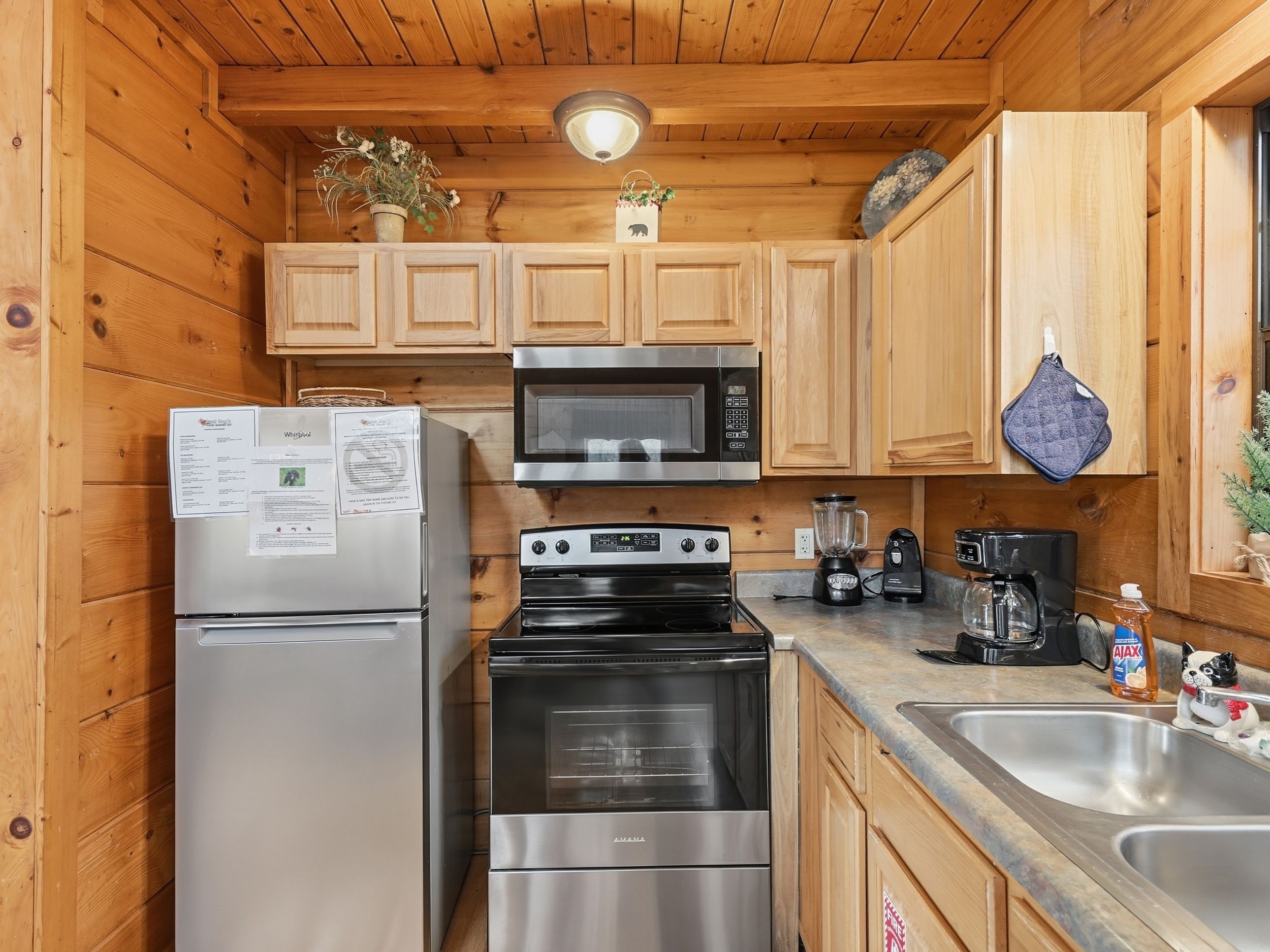 A compact kitchen with wooden cabinets, a stainless steel refrigerator, a microwave, a stove, and a sink.