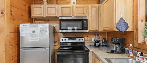 A compact kitchen with wooden cabinets, a stainless steel refrigerator, a microwave, a stove, and a sink.