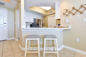 A kitchen with white cabinets, a stainless steel refrigerator, and two bar stools with cushioned seats. - Serene Beachfront Condo w/ Gulf Views & Close Dining in The Heart of Destin! 💙☀ (Destin)