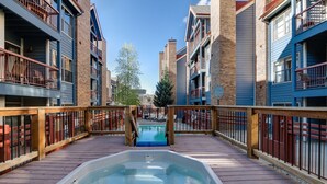 Una terraza de madera con un jacuzzi, rodeada de edificios de varios pisos con balcones y barandillas.