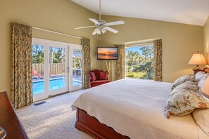 A bedroom with a bed, a ceiling fan, a TV, and a view of a pool.