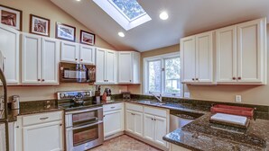 Una cocina con armarios blancos, encimeras de granito, un tragaluz y una ventana.