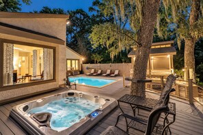 A hot tub and a swimming pool on a wooden deck with lounge chairs and a covered seating area.