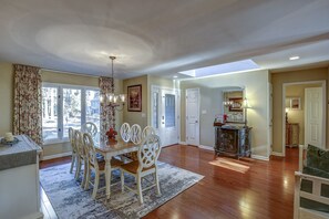 A dining area with a glass-top table, white chairs, and a chandelier.