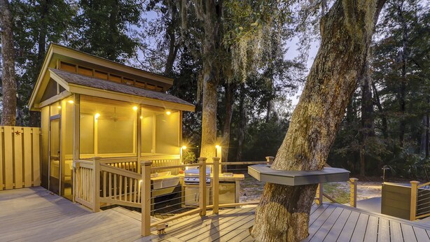 Una terraza de madera con una estructura cubierta de vidrio, posiblemente un spa o sauna, rodeada de árboles.