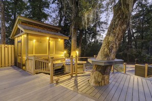 A wooden deck with a glass-enclosed structure, possibly a spa or sauna, surrounded by trees.