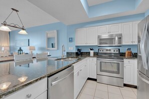 Een moderne keuken met witte kasten, roestvrijstalen apparatuur, een granieten aanrechtblad en een blauwe accentmuur.