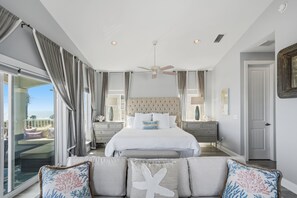Une chambre avec un grand lit, un ventilateur de plafond et une vue sur l’extérieur, visible à travers la porte vitrée.