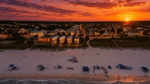 Une ville côtière au coucher du soleil, avec des propriétés situées en bord de mer et des personnes se promenant sur la plage.