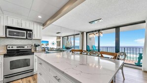 A modern kitchen with a large island, white cabinetry, and a view of the ocean. - BeachFront for 8~Remodeled~Pool~2BR Edgewater 611 Tower 2 (Panama City Beach)