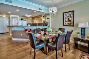 A modern kitchen with wooden cabinets, a dining area with a glass table and leather chairs, and a chandelier. - INCREDIBLE VIEWS! SLEEPS 8! LUXURY CONDO! (Panama City Beach)